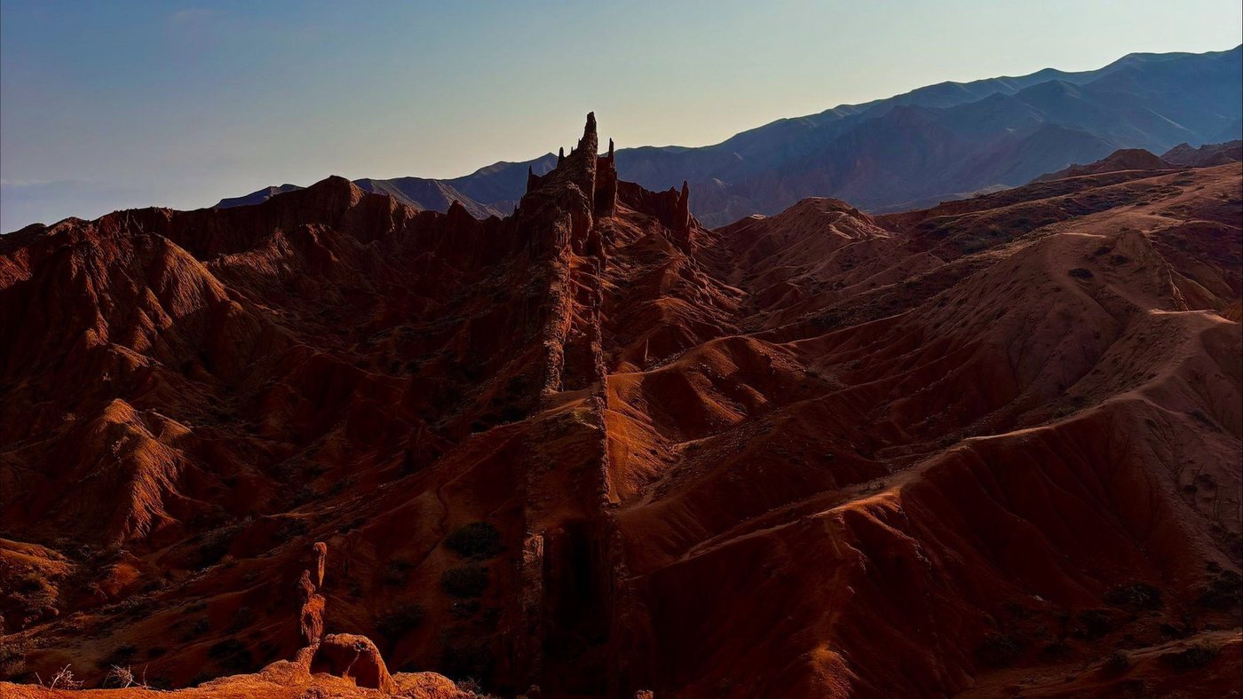 Red sandstone spires and a long fin of rock at Fairy Tale Canyon, with the mountains of the Issyk-Kul basin behind.