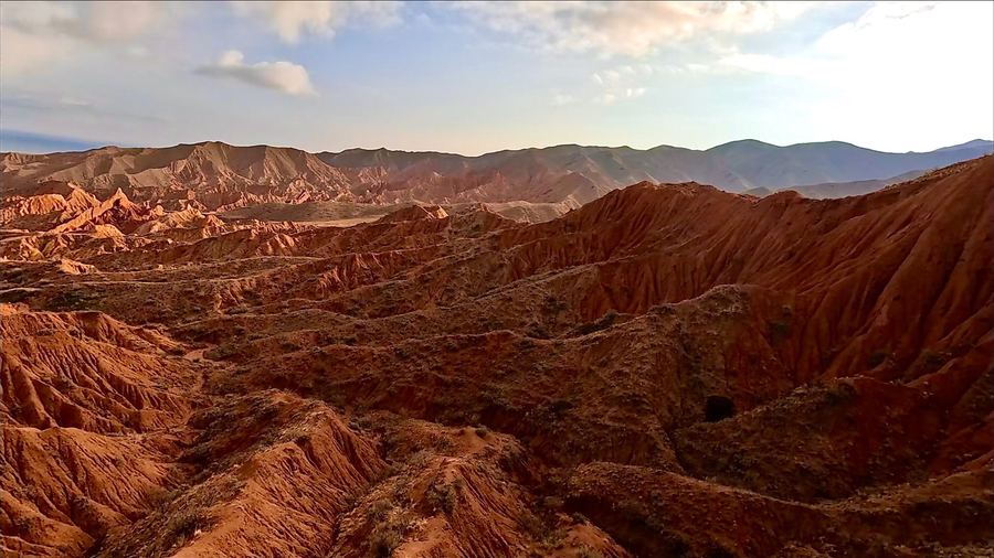 The eroded red badlands of Fairy Tale Canyon at low sun, ridges and gullies running towards distant hills.
